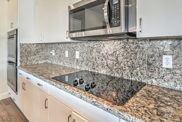 kitchen with appliances with stainless steel finishes, light stone countertops, decorative backsplash, dark hardwood / wood-style flooring, and white cabinetry