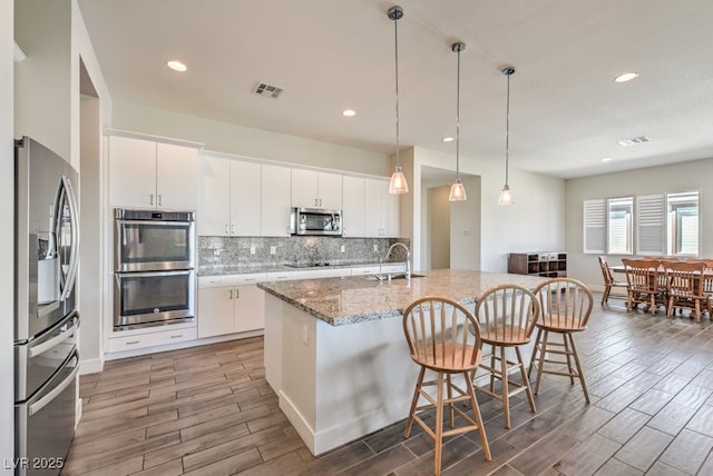 kitchen featuring white cabinets, appliances with stainless steel finishes, and a center island with sink