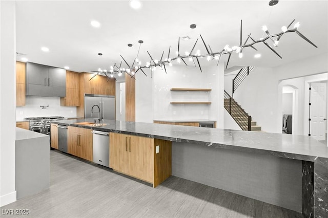 kitchen featuring a large island with sink, pendant lighting, dark stone counters, and appliances with stainless steel finishes