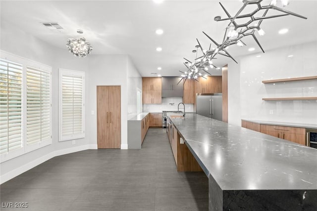 kitchen featuring pendant lighting, an inviting chandelier, a large island with sink, and built in refrigerator