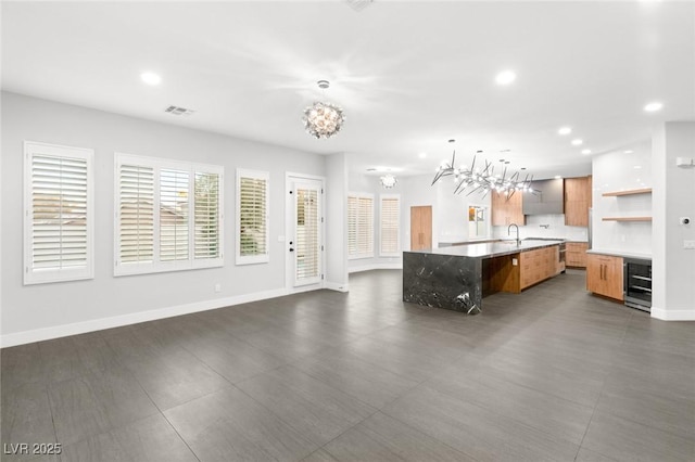 kitchen featuring a center island with sink, hanging light fixtures, beverage cooler, sink, and a kitchen bar