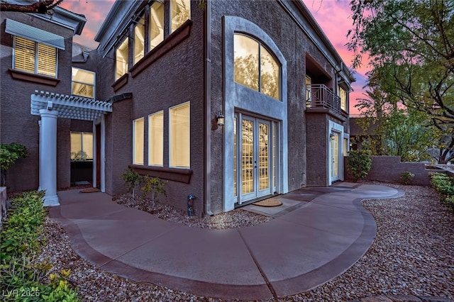 property exterior at dusk with a pergola, a garage, french doors, and a balcony