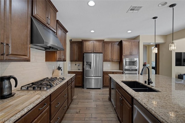 kitchen featuring stainless steel appliances, visible vents, a sink, wood finished floors, and under cabinet range hood