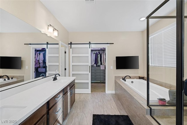 full bathroom featuring double vanity, a garden tub, a walk in closet, and a sink