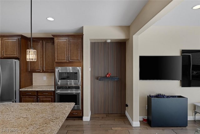 kitchen featuring baseboards, wood finished floors, light stone countertops, stainless steel appliances, and backsplash