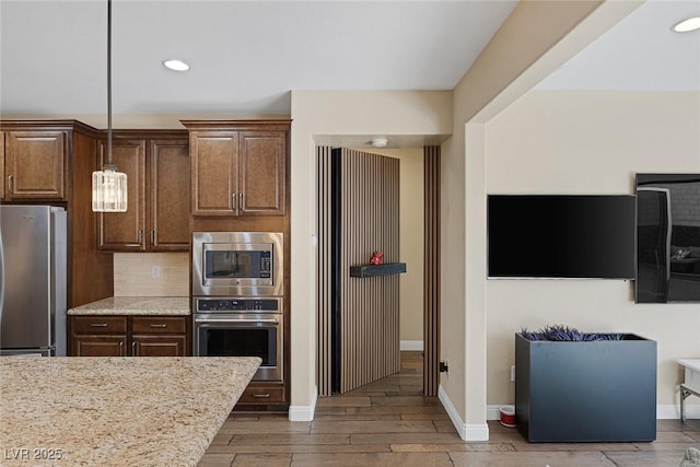 kitchen featuring light stone counters, wood finish floors, baseboards, appliances with stainless steel finishes, and backsplash