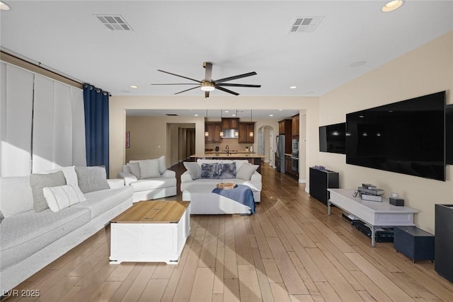 living area featuring arched walkways, ceiling fan, visible vents, and light wood-style floors