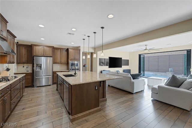 kitchen featuring under cabinet range hood, a sink, open floor plan, appliances with stainless steel finishes, and light wood-type flooring