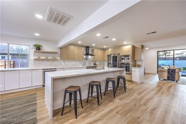 kitchen featuring appliances with stainless steel finishes, a breakfast bar area, wall chimney range hood, and a center island with sink