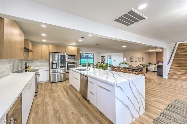 kitchen featuring a center island with sink, stainless steel appliances, light stone counters, white cabinets, and sink