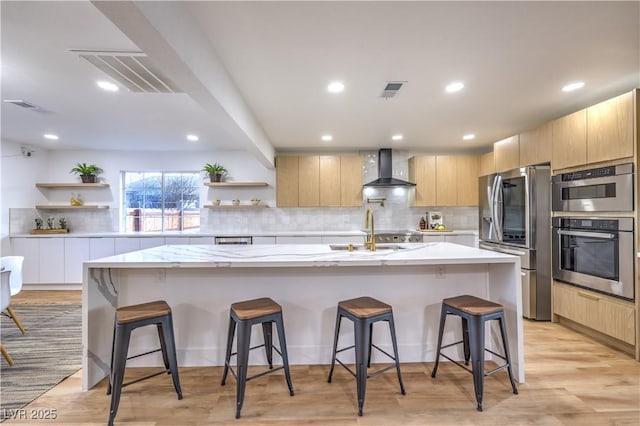 kitchen with wall chimney range hood, a center island with sink, appliances with stainless steel finishes, and a breakfast bar