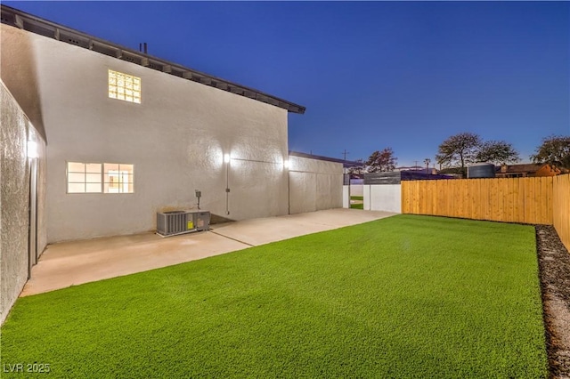 back house at dusk with a yard, a patio, and central air condition unit