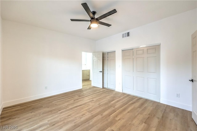 unfurnished bedroom featuring ceiling fan, two closets, and light wood-type flooring