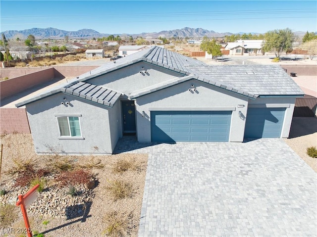 ranch-style home featuring an attached garage, a mountain view, decorative driveway, and stucco siding