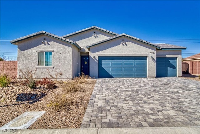 ranch-style house featuring a garage, decorative driveway, a tile roof, and stucco siding