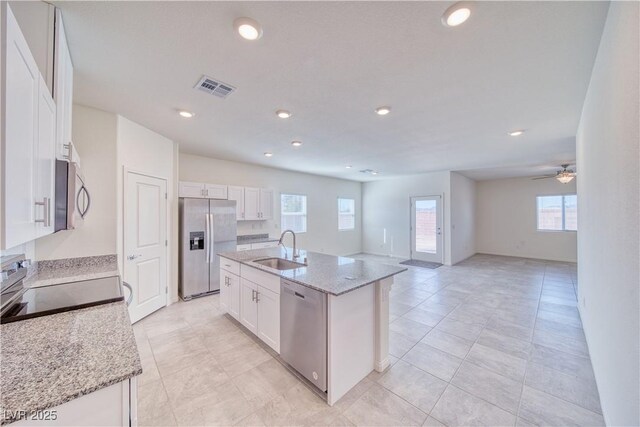 kitchen with white cabinets, an island with sink, open floor plan, stainless steel appliances, and a sink