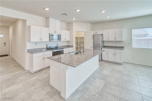 kitchen with stainless steel appliances, a kitchen island with sink, a sink, and white cabinetry