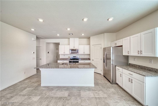 kitchen with light stone counters, a center island with sink, appliances with stainless steel finishes, white cabinetry, and a sink