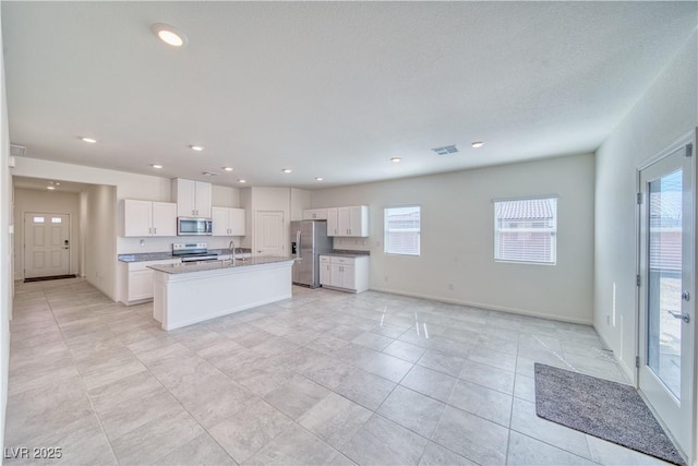 kitchen with stainless steel appliances, a sink, white cabinetry, a healthy amount of sunlight, and a center island with sink