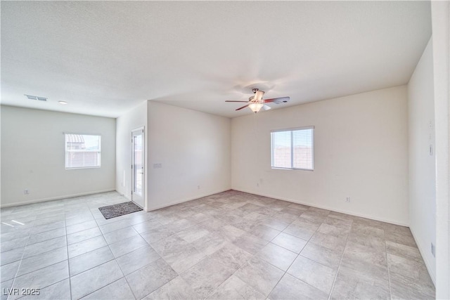 spare room featuring a wealth of natural light, visible vents, ceiling fan, and baseboards