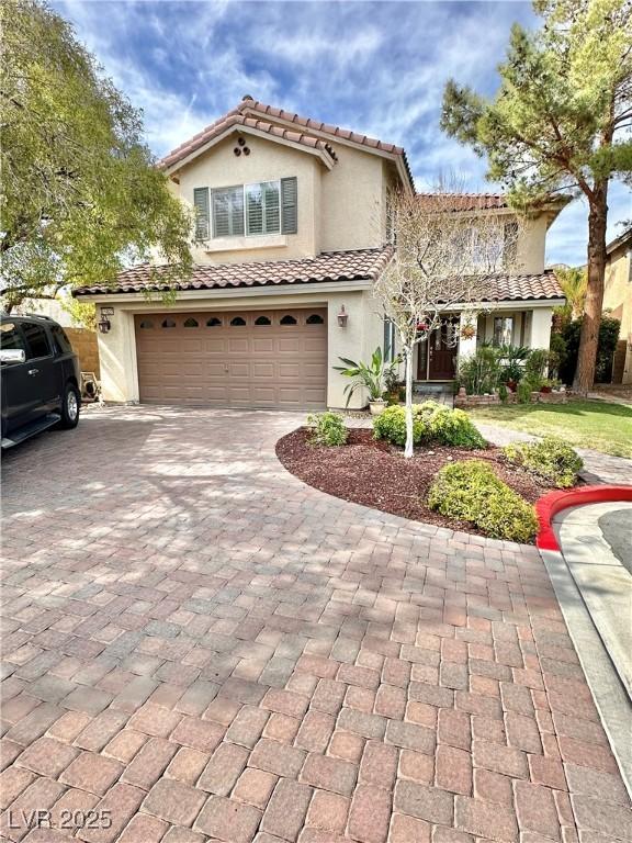 mediterranean / spanish-style house with a garage, decorative driveway, and stucco siding