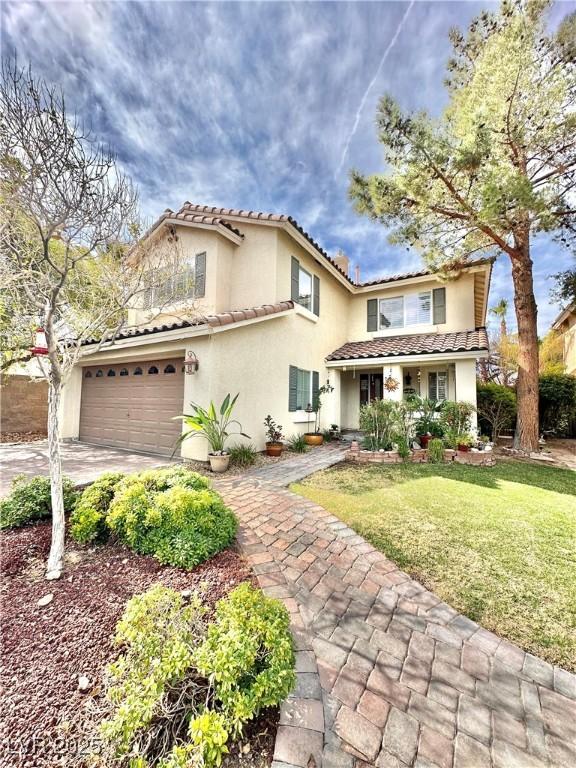 mediterranean / spanish-style home with a garage, driveway, stucco siding, a tiled roof, and a front yard