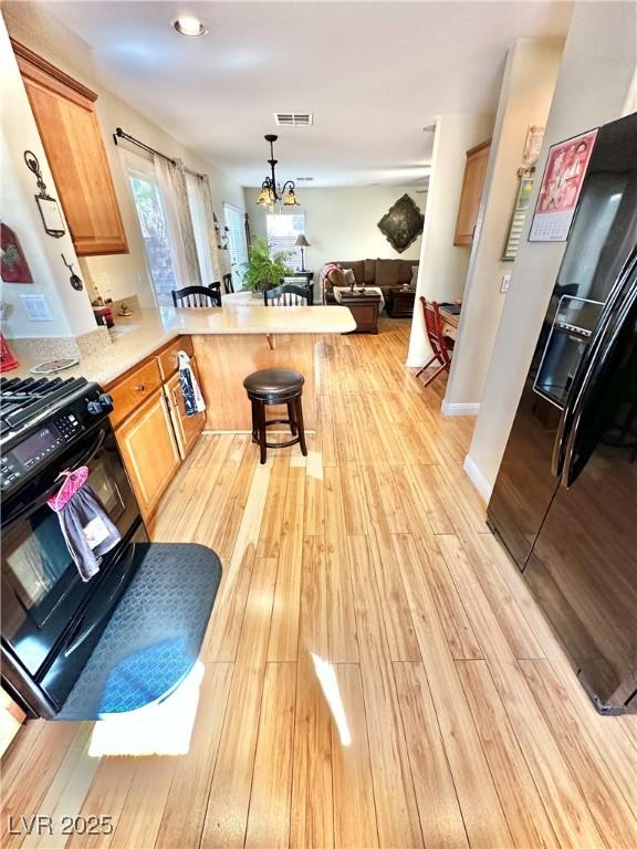 kitchen featuring a peninsula, a breakfast bar, visible vents, light wood-type flooring, and black appliances