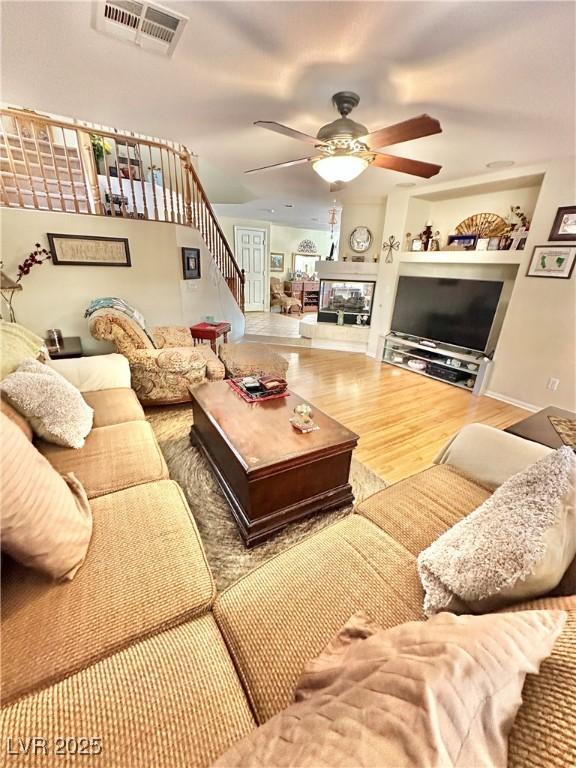 living room featuring stairs, a ceiling fan, visible vents, and wood finished floors