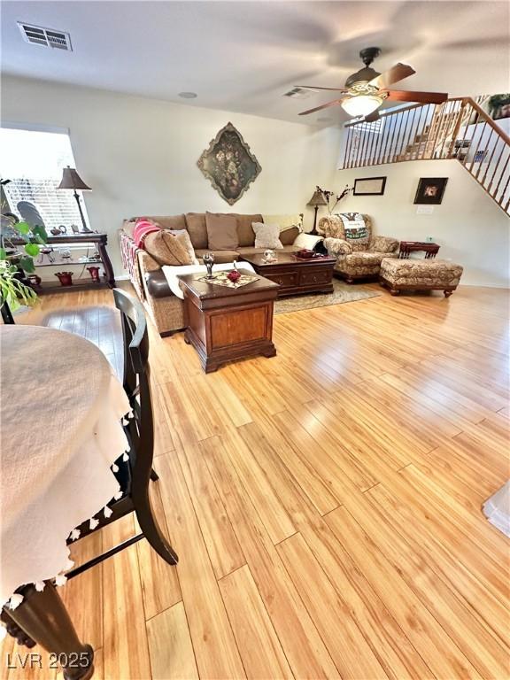 living room with visible vents, ceiling fan, light wood-style flooring, and stairs