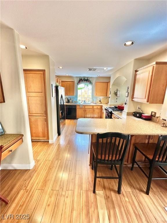 kitchen featuring light wood-style flooring, a peninsula, black dishwasher, freestanding refrigerator, and a kitchen bar