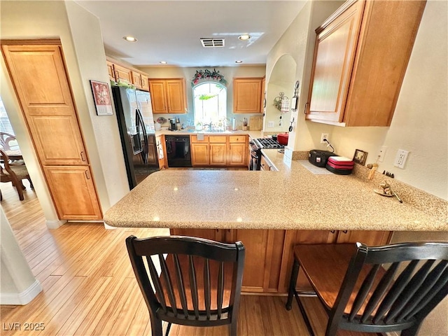 kitchen with visible vents, black appliances, light wood-type flooring, a peninsula, and a kitchen bar