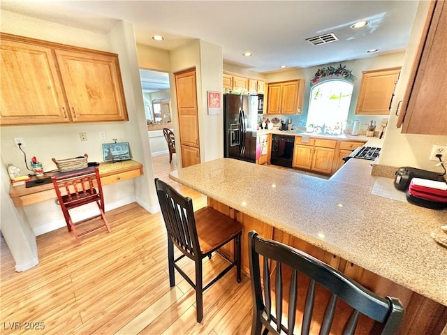 kitchen featuring light wood-style flooring, a peninsula, visible vents, black appliances, and a kitchen bar