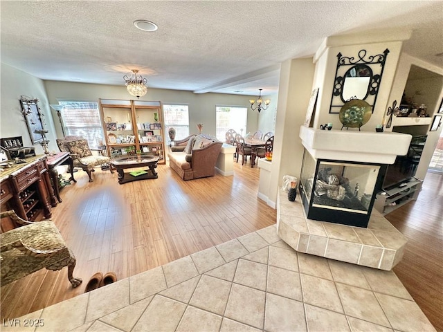 living room with a chandelier, a textured ceiling, a multi sided fireplace, and wood finished floors