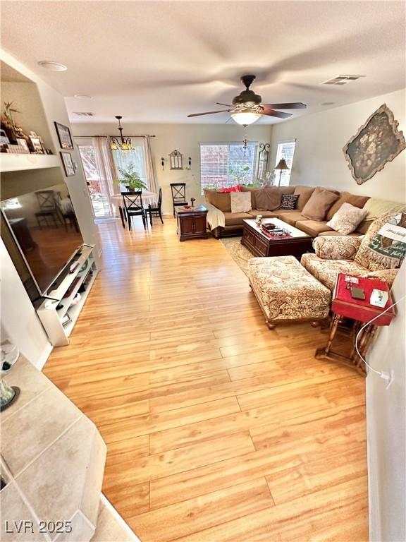 living area featuring light wood-style floors, visible vents, and ceiling fan with notable chandelier