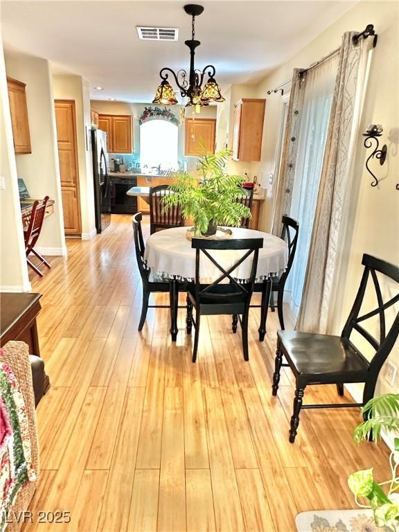 dining space with a chandelier, light wood finished floors, visible vents, and baseboards