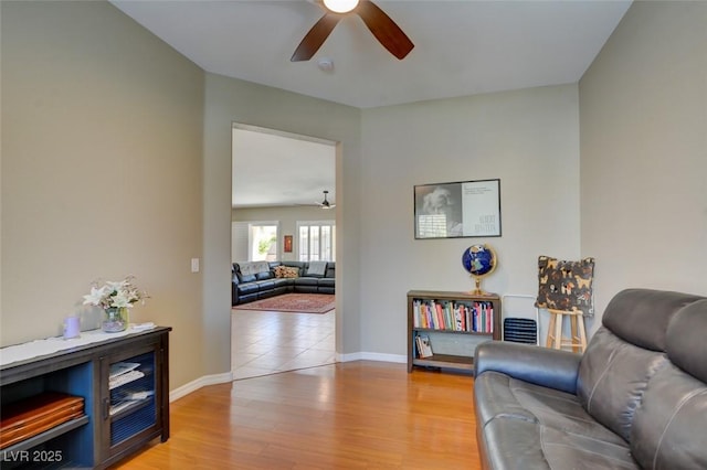 living area with a ceiling fan, light wood-style flooring, and baseboards