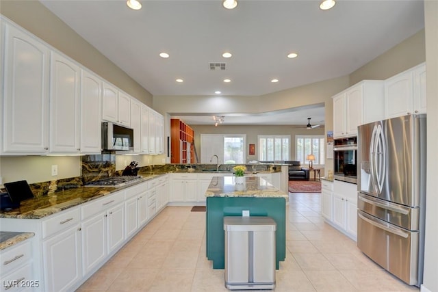 kitchen featuring visible vents, a center island, a peninsula, stainless steel appliances, and a sink