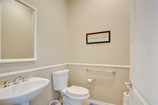 half bath featuring toilet, baseboards, and a sink