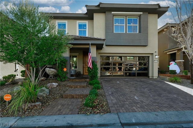 view of front of house with decorative driveway, an attached garage, and stucco siding