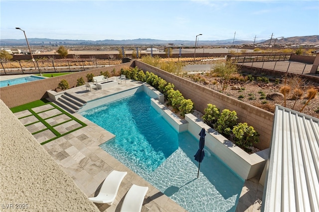 view of swimming pool featuring a rural view, a fenced in pool, a fenced backyard, a patio area, and a mountain view