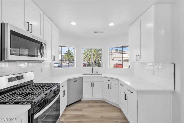 kitchen featuring appliances with stainless steel finishes, light hardwood / wood-style flooring, sink, and white cabinets