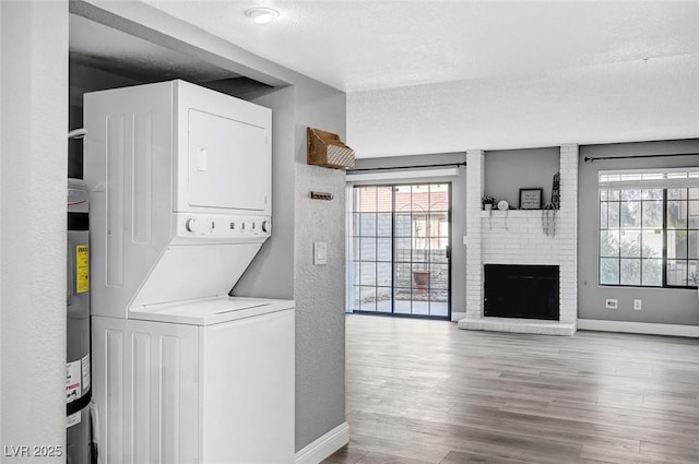 washroom with a brick fireplace, light wood-type flooring, a textured ceiling, water heater, and stacked washer / drying machine