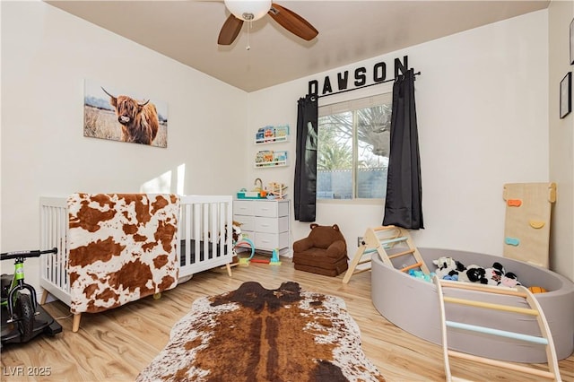 bedroom featuring ceiling fan, a crib, and wood-type flooring