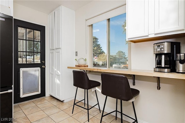 kitchen featuring butcher block countertops, white cabinets, a breakfast bar, light tile patterned floors, and black fridge