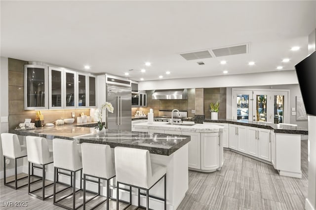 kitchen featuring kitchen peninsula, a spacious island, stainless steel built in refrigerator, white cabinets, and a kitchen bar