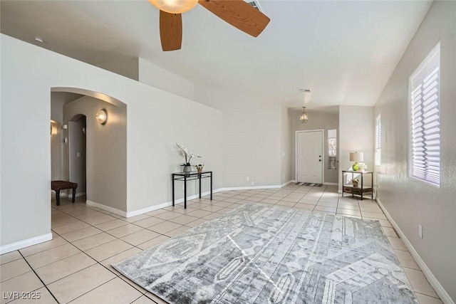 interior space with arched walkways, ceiling fan, baseboards, and light tile patterned floors