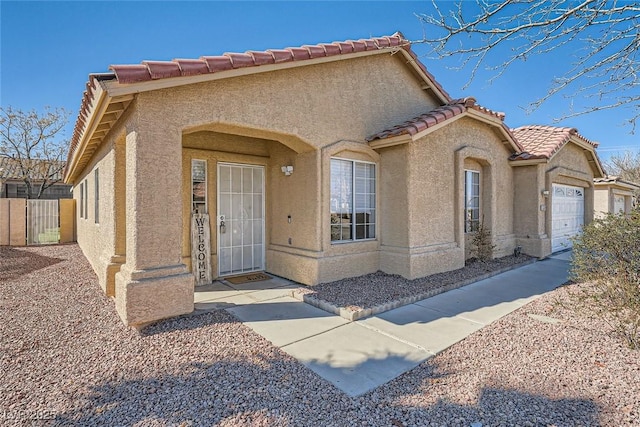 mediterranean / spanish-style house with an attached garage, a tiled roof, fence, and stucco siding