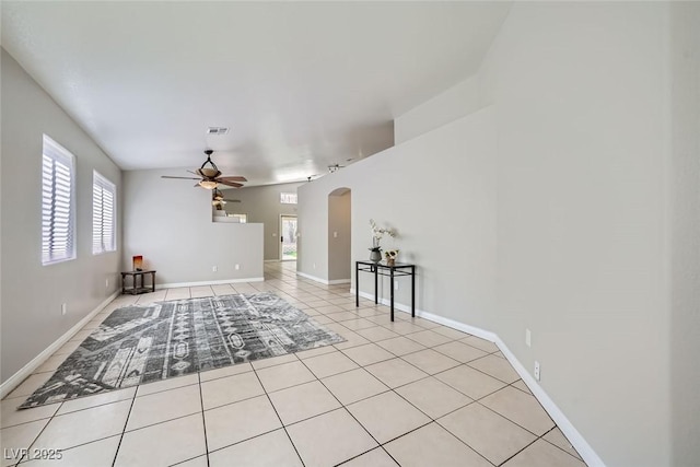 interior space featuring arched walkways, light tile patterned floors, visible vents, a ceiling fan, and baseboards