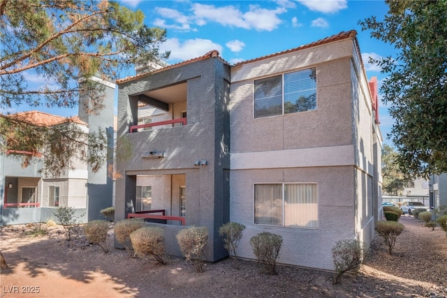 exterior space with a tile roof, a balcony, and stucco siding