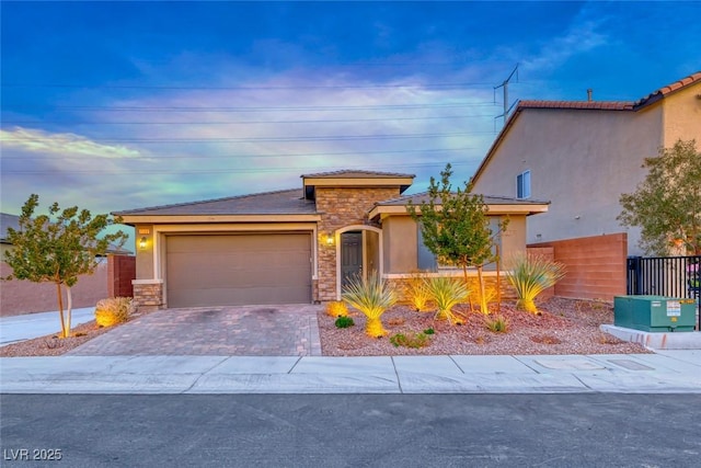 view of front of house featuring a garage, stone siding, fence, decorative driveway, and stucco siding